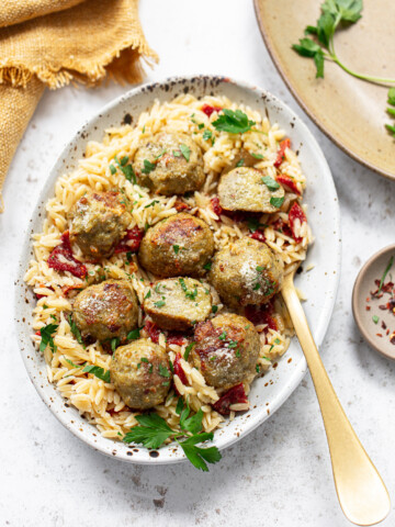 Chicken meatballs and orzo on a platter, with a spoon on the side.