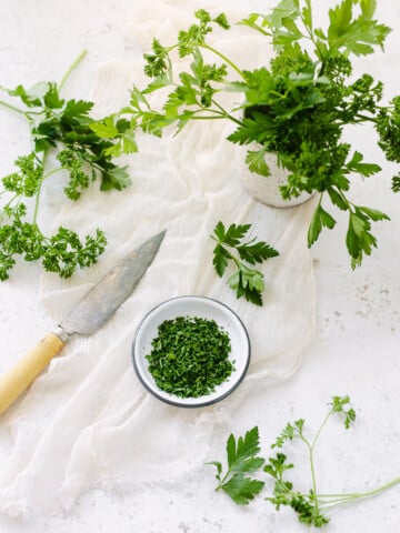 A dish of chopped parsley on a surface, surrounded by random parsley leaves and a knife.