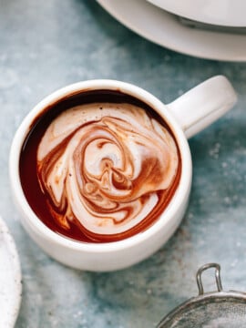 A mug of hot chocolate with a decorative layer of cream on top.