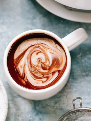 A mug of hot chocolate with a decorative layer of cream on top.