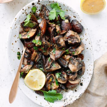 Roasted mushrooms on a serving platter garnished with lemon and parsley leaves.
