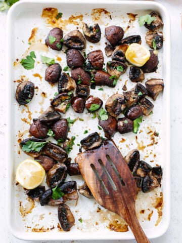 Roasted mushrooms on a sheet pan, with lemon wedges and a spatula.
