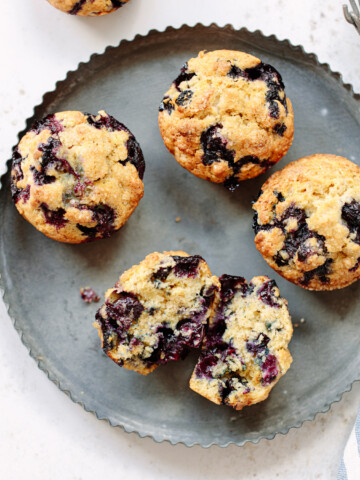One split and three whole blueberry muffins on a round tin.