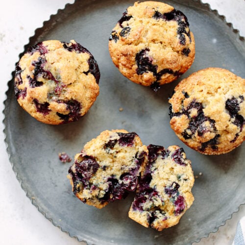 One split and three whole blueberry muffins on a round tin.