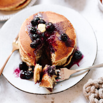 A stack of pancakes and a fork on a plate with butter and blueberry sauce on top.