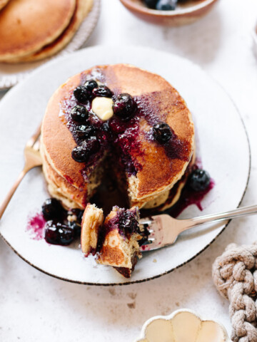 A stack of pancakes and a fork on a plate with butter and blueberry sauce on top.