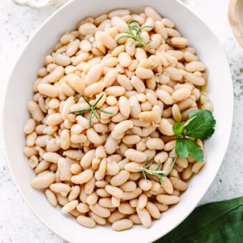 Cooked cannellini beans on a platter, topped with fresh herb sprigs.