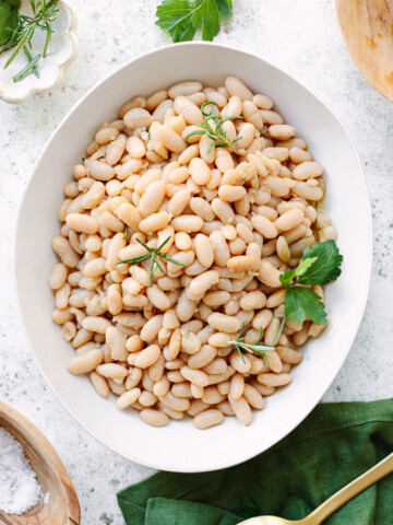 Cooked cannellini beans on a platter, topped with fresh herb sprigs.