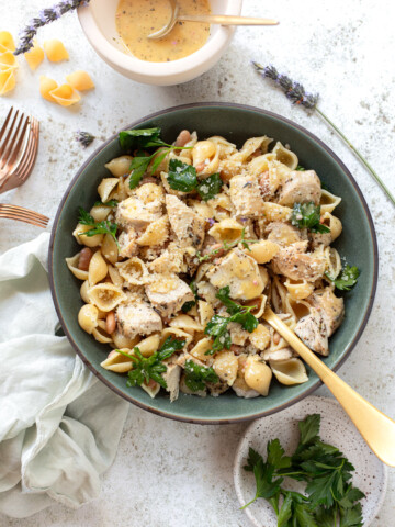 Sliced chicken and pasta shells in a salad bowl, with a serving spoon, and napkins and forks surrounding the bowl.