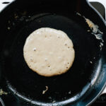 Pancake batter sizzling on a cast iron skillet.