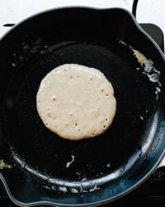Pancake batter sizzling on a cast iron skillet.