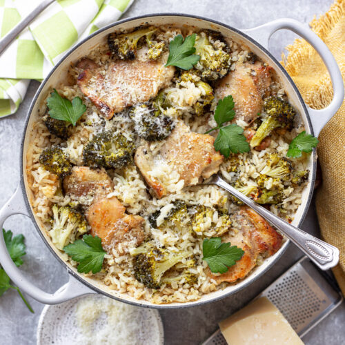 Pieces of baked boneless chicken in a skillet with a serving spoon, on top of rice and broccoli.