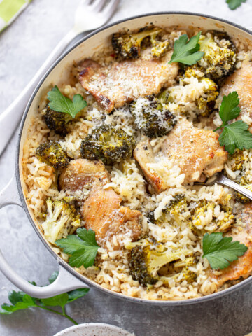 Boneless chicken thighs being served in a skillet, with baked rice and cheese-topped broccoli florets.