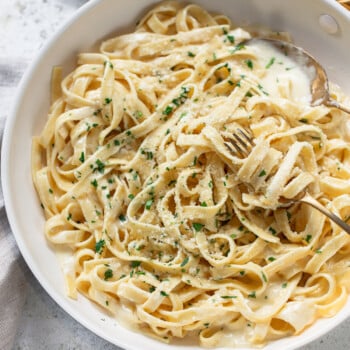 Fettuccine pasta noodles in a pan with cream sauce, with a fork and spoon.