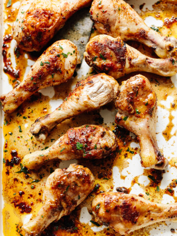Juicy browned, spice-rubbed chicken legs on a white baking sheet.
