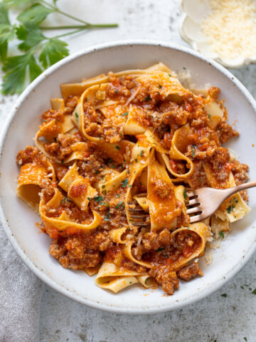 Fettuccine with meaty sauce in a serving bowl, with a fork twirled around some noodles.