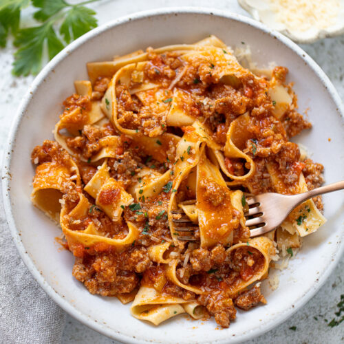 Fettuccine with meaty sauce in a serving bowl, with a fork twirled around some noodles.
