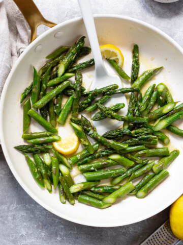 Sliced asparagus in a saute pan with a spatula and lemon wedges.