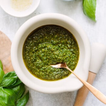 Fresh basil pesto sauce in a ceramic bowl, with a spoon dipping into it.
