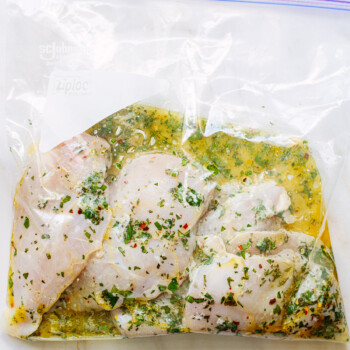 Boneless, skinless chicken breasts in a freezer bag, marinating in an herb and olive oil mixture.