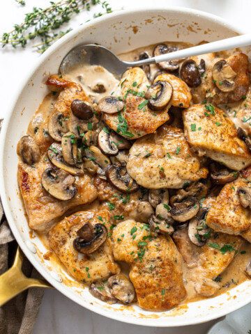 Golden brown chicken breast pieces in a skillet, with mushrooms and cream sauce