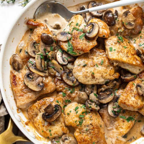 Golden brown chicken breast pieces in a skillet, with mushrooms and cream sauce