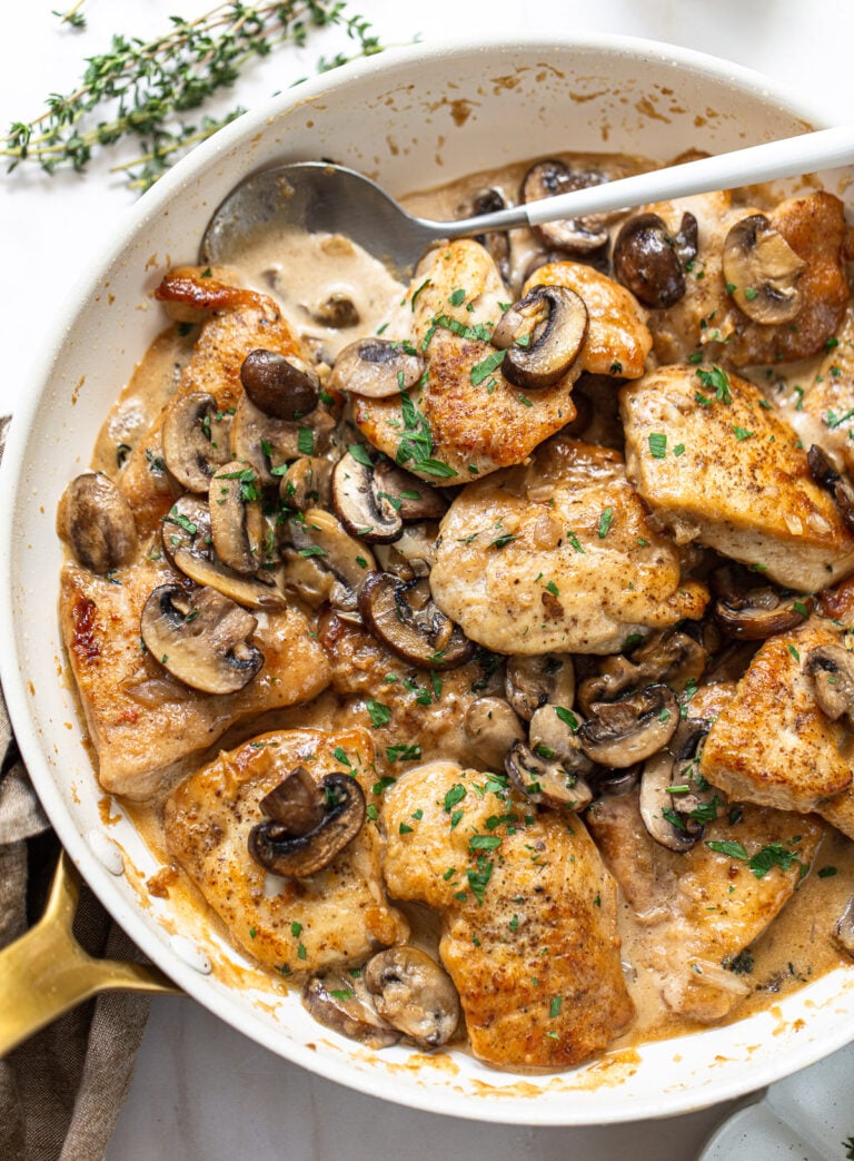 Golden brown chicken breast pieces in a skillet, with mushrooms and cream sauce