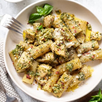 Prepared pasta with pesto chicken sauce in a serving bowl, with sprigs of fresh basil and forks on the side.