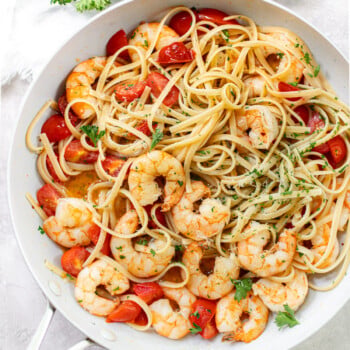 Cooked shrimp and linguine pasta in garlic butter sauce and chopped parsley in a skillet.