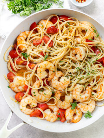 Cooked shrimp and linguine pasta in garlic butter sauce and chopped parsley in a skillet.