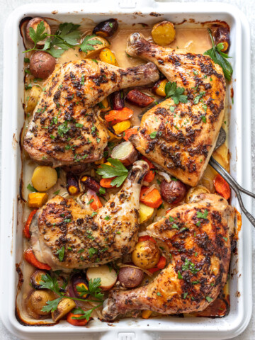 Baked chicken leg quarters and a metal spatula on a sheet pan on top of roasted vegetables.