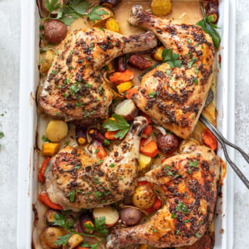 Baked chicken leg quarters on a sheet pan on top of roasted vegetables.