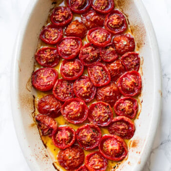 Roasted cherry tomatoes with olive oil in an oval baking dish.