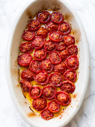 Roasted cherry tomatoes with olive oil in an oval baking dish.