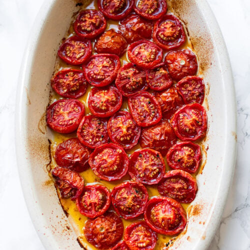 Roasted cherry tomatoes with olive oil in an oval baking dish.
