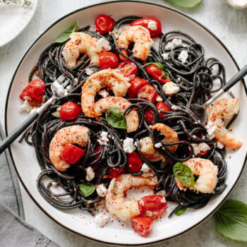A plate of squid ink pasta with shrimp, tomato and basil sauce.