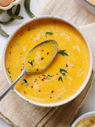 Smooth butternut squash soup in a bowl, with a spoon propped on the side of the bowl.
