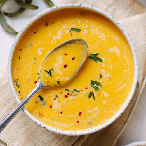 Smooth butternut squash soup in a bowl, with a spoon propped on the side of the bowl.