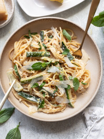 Lemon pasta with zucchini, basil and parmesan shreds in a bowl, with two forks on either side.