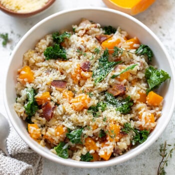 A bowl of risotto strewn with cubed butternut squash, kale leaves and crisp bacon.