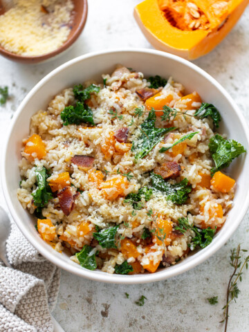 A bowl of risotto strewn with cubed butternut squash, kale leaves and crisp bacon.