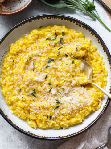 Golden yellow arborio rice risotto in a serving bowl, with a spoon dipping in for a portion.