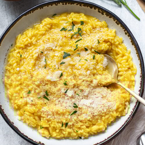 Golden yellow arborio rice risotto in a serving bowl, with a spoon dipping in for a portion.