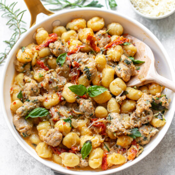 Cooked gnocchi in a skillet, in a sauce including sliced sausage, tomatoes, basil and grated cheese.