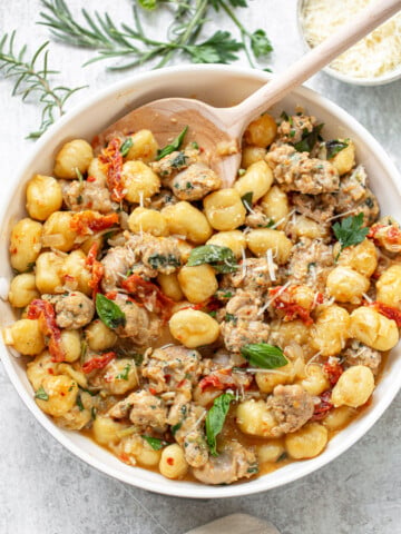 Cooked gnocchi dinner in a skillet, in a sauce including sliced Italian sausage, tomatoes, basil and grated cheese.