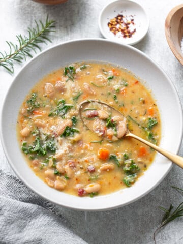 White bean soup sprinkled with rosemary leaves in a serving bowl with a spoon inside.