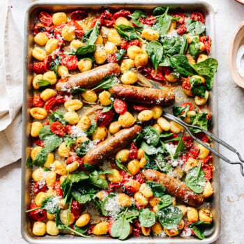 Baked whole Italian sausage and gnocchi sheet pan dinner with grated cheese and spinach leaves on top and a spatula for serving.