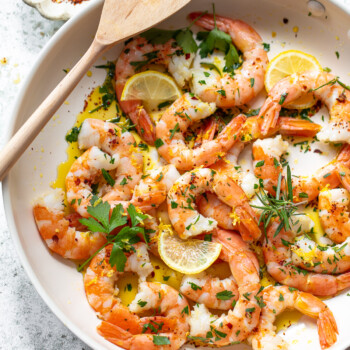 Sauteed pink shrimp with olive oil, garlic and herbs arranged in a skillet, and a spatula resting on the side of the pan.