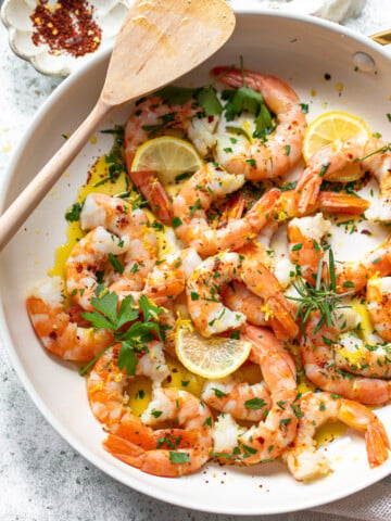 Sauteed pink shrimp with olive oil, garlic and herbs arranged in a skillet, and a spatula resting on the side of the pan.