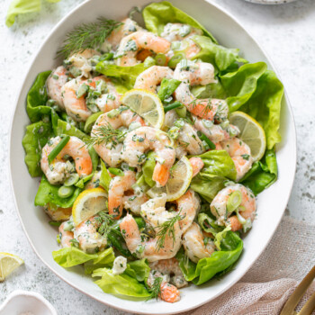 A platter of shrimp salad with layers of butter lettuce, shrimp, herbs and lemon slices.